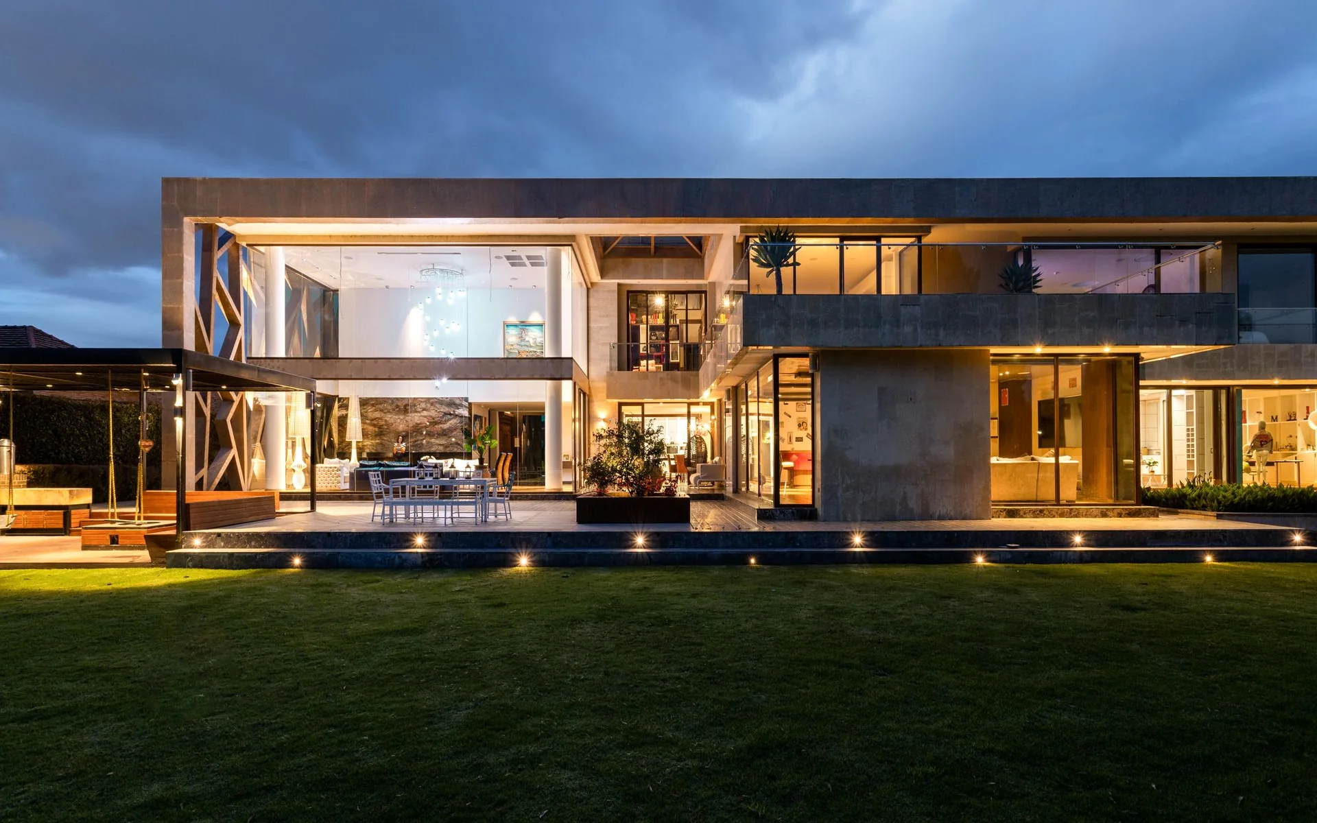 Casa moderna de dos niveles con grandes ventanales de vidrio al atardecer