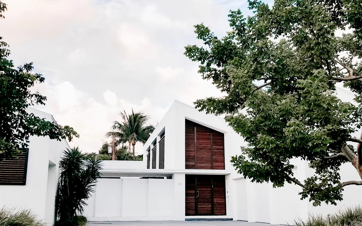 Fachada blanca de casa moderna con puertas de madera y palmeras